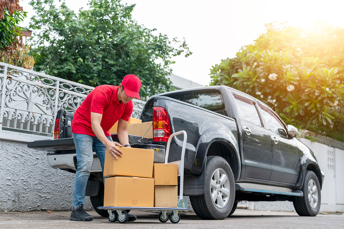 Delivery-men-in-red-uniform-unloading-cardboard-boxes-from-pickup-truck